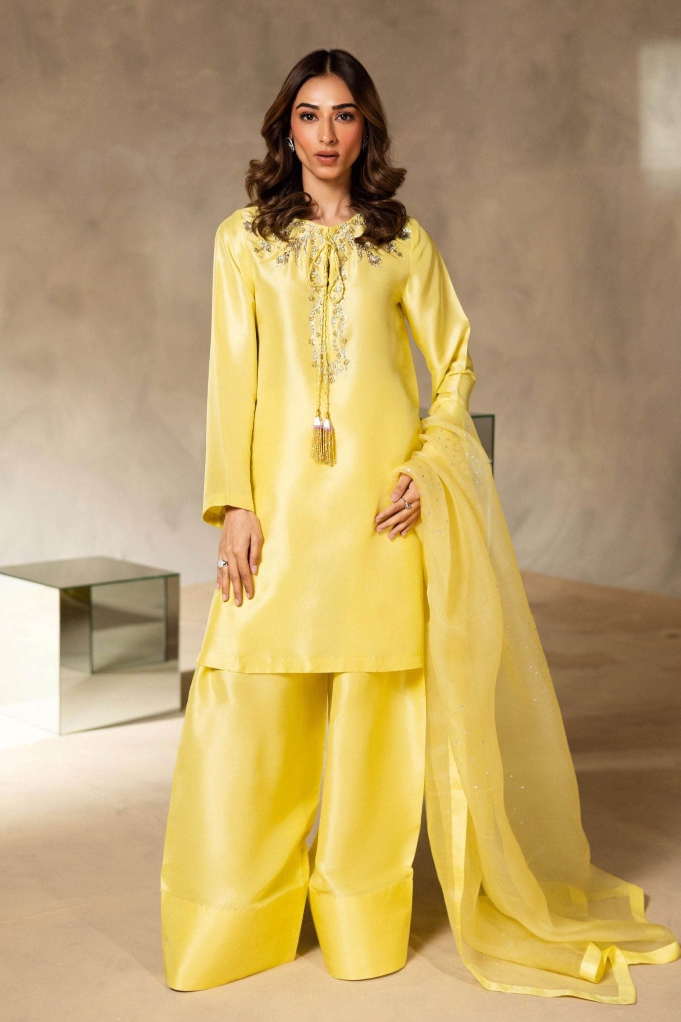 Woman in a bright yellow traditional outfit standing against a neutral background